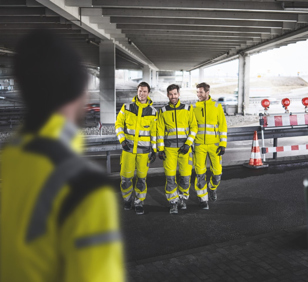 Ein Mann blickt auf 3 weitere Männer die den gleichen Warnanzug tragen wie er
