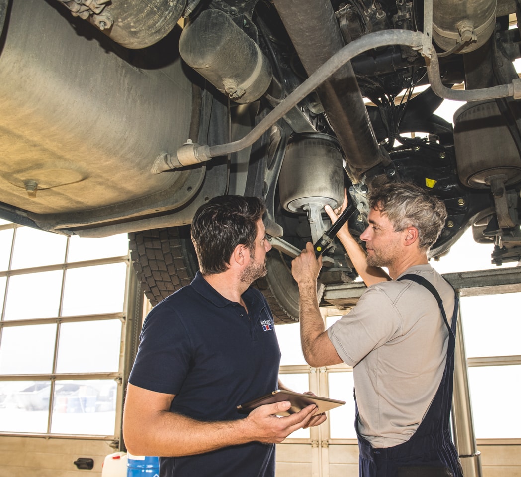 2 Männer unter einem LKW schauen sich einen Luftfederbalg an